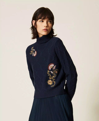 Model wearing the Twinset 100% wool turtleneck sweater with floral embroidery, textured Aran-inspired knit and ribbed detailing.
