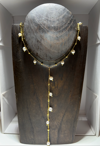 Gold Y-shaped necklace with delicate white pearl drops and gold bead accents displayed on a dark wood jewelry stand.
