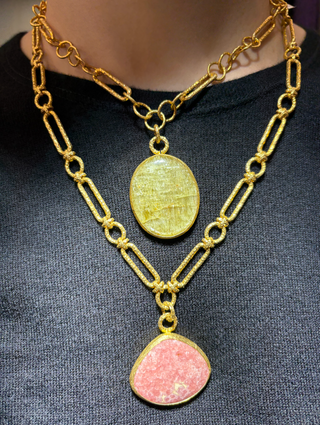 Layered gold chain necklaces featuring oval pink and cat-eye natural stone pendants, styled over a black top.