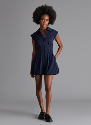 Woman wearing a navy sleeveless zip front bubble hem mini dress with a collared neckline and fitted waist.