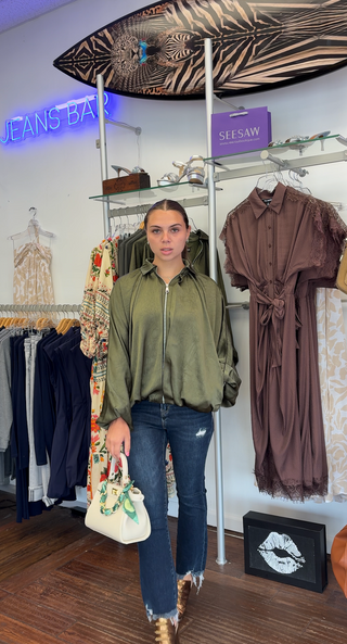 Woman wearing an oversized olive green zip front bomber jacket with dropped shoulders and a relaxed fit.