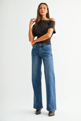 Woman wearing mid-rise wide-leg jeans with metallic stud detailing along the sides