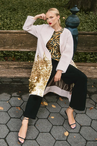 Woman sitting on a bench wearing a stylish outfit with a gold sequin jacket.