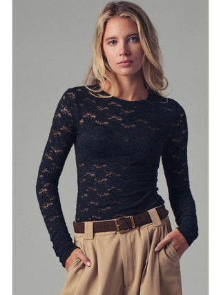 Woman wearing a black lace top and beige pants against a gray background